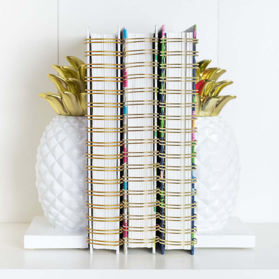Daily Simplified Planners on a shelf between two white and gold pineapple bookends