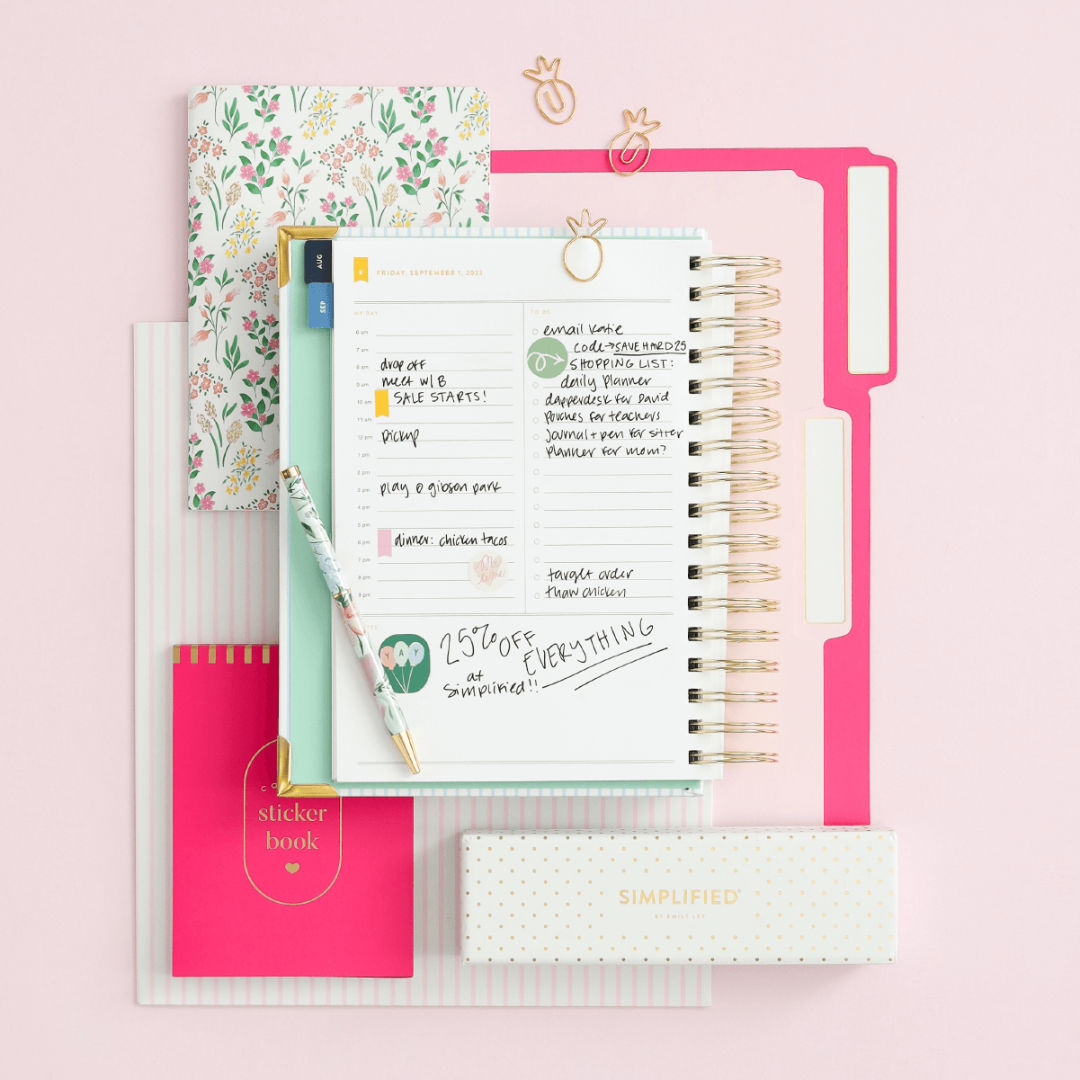 various Simplified products including a Daily Simplified Planner, mini notebook, file folders, sticker book, and pens arranged in a flat lay on a pick background